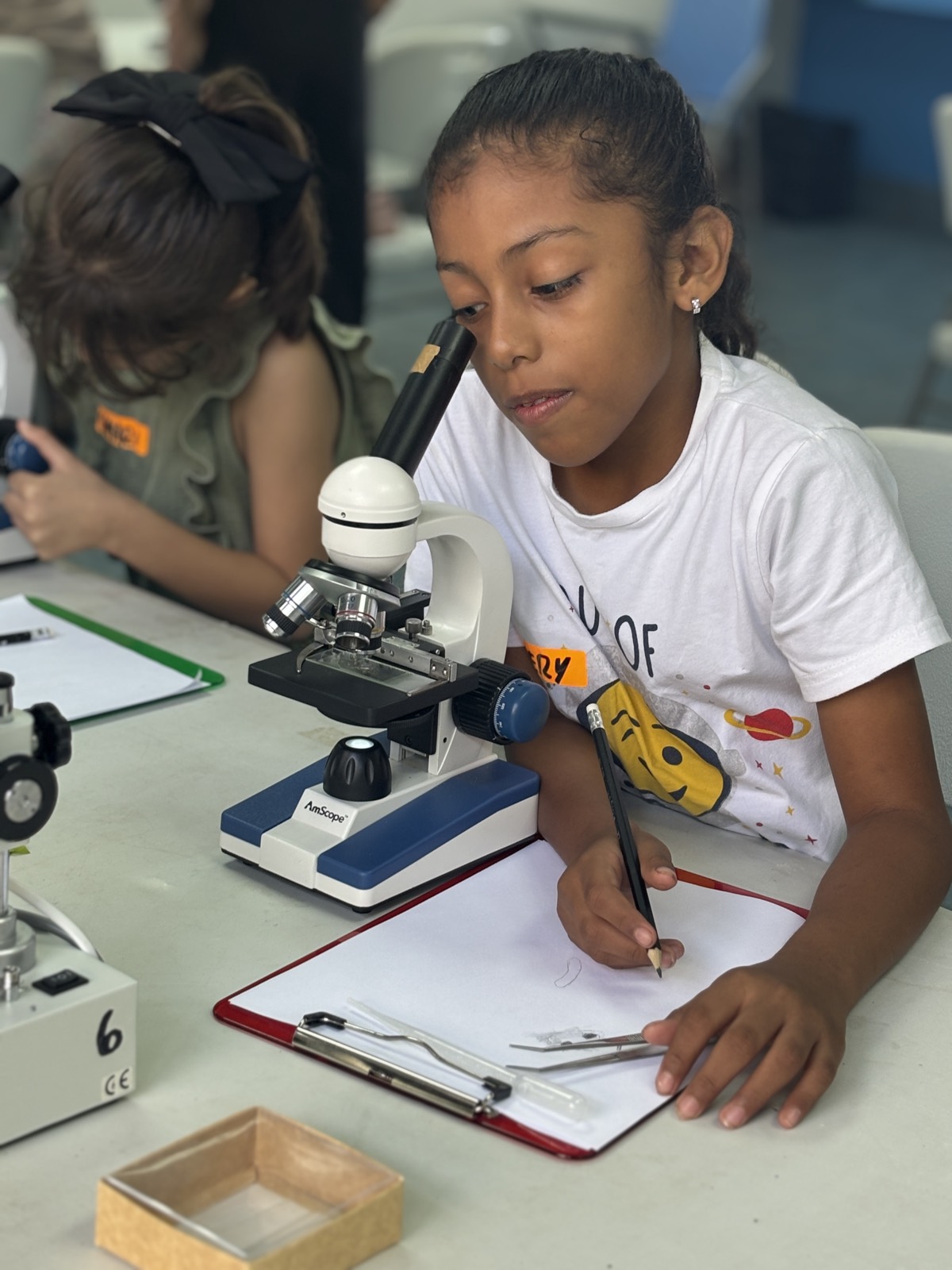 Una niña anota sus observaciones junto a un microscopio